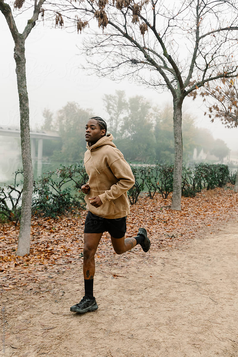 A black man runs on the trails of a public park on a foggy morning