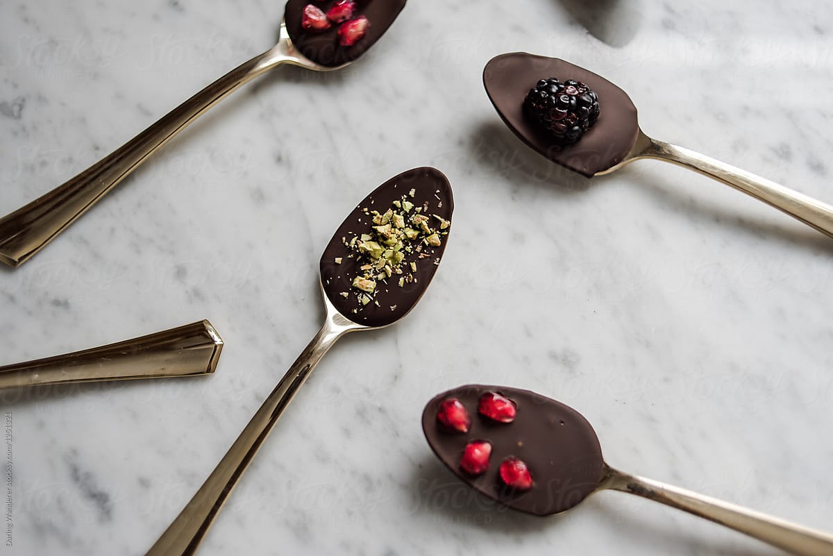 Health dark chocolate covered gold spoons with pomegranate seeds, pistachios and blackberries
