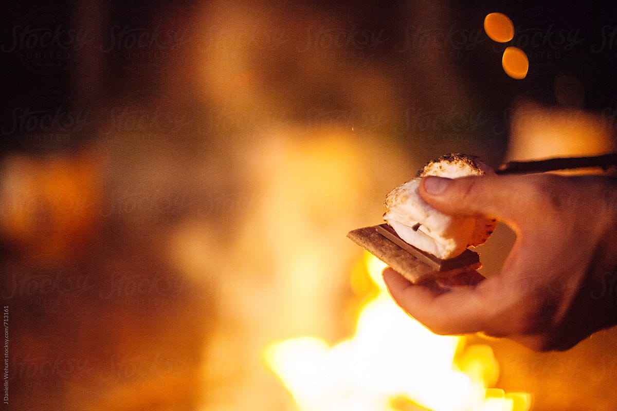 A caucasian hand placing roasted marshmallows on a graham cracker making s\'mores.