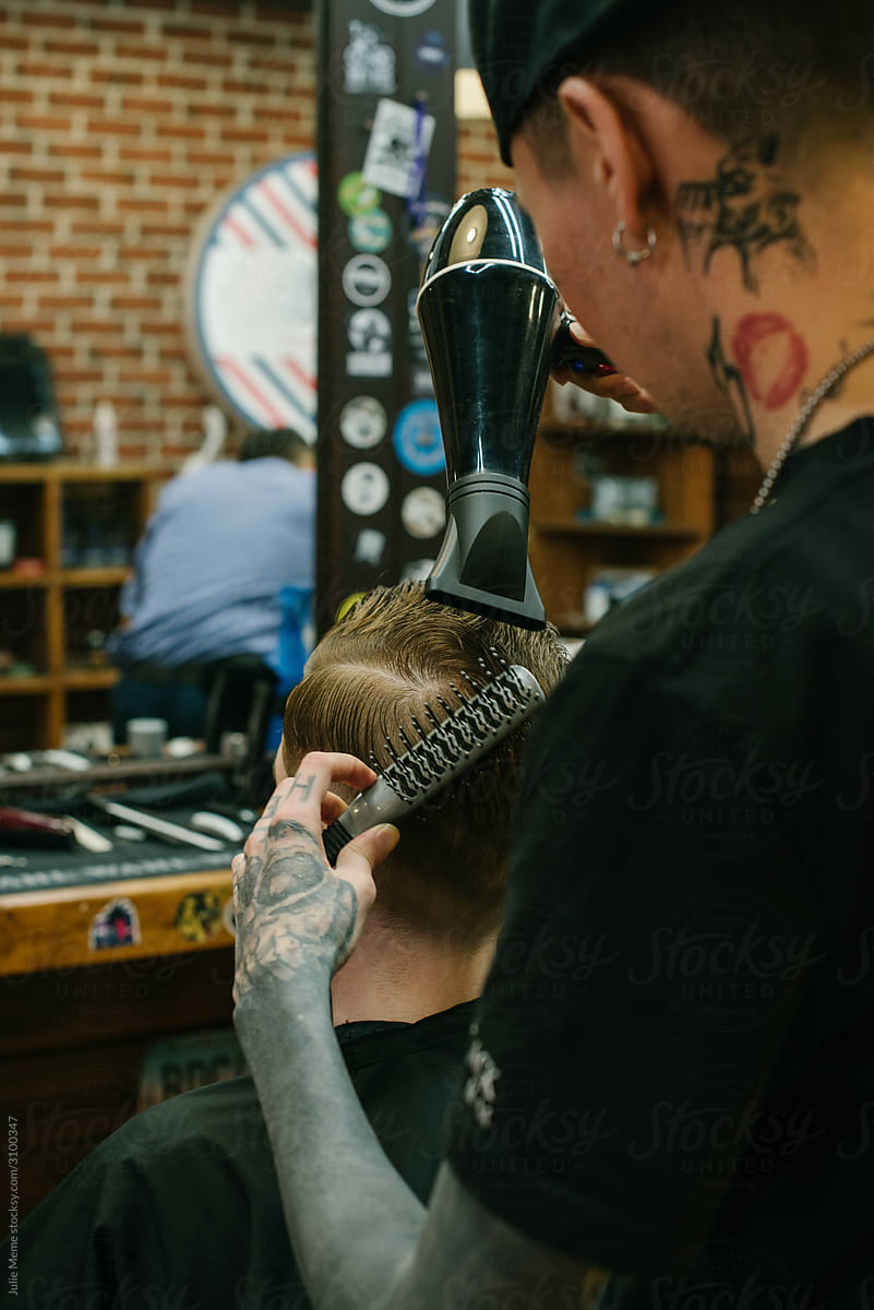 A tattooed barber works with a client