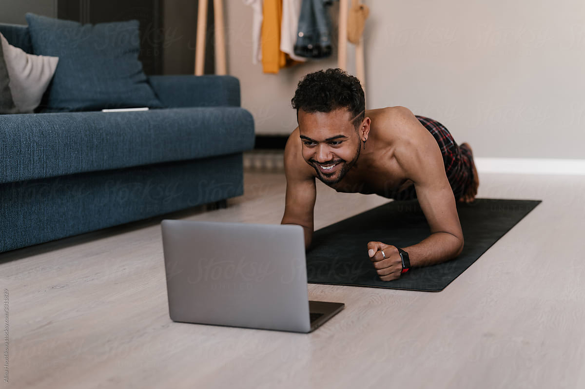 Ethnic man doing plank during online workout