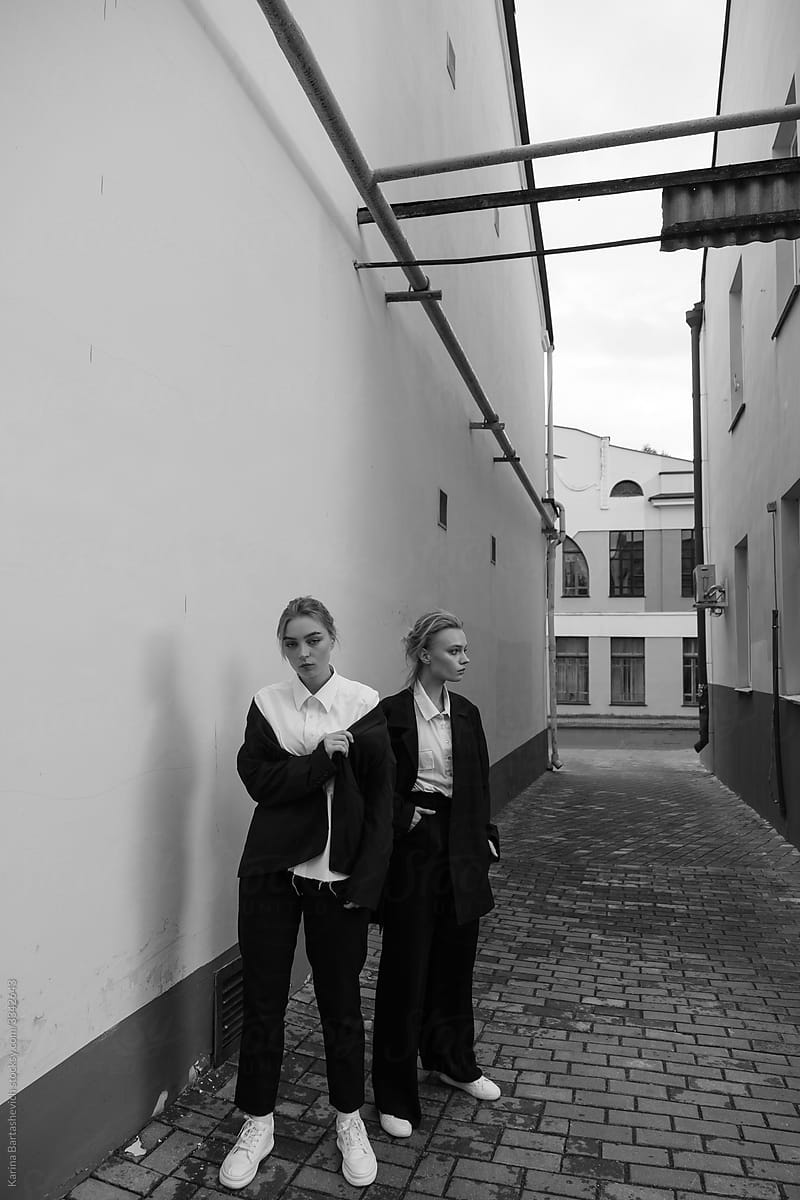 black and white photo of two sisters in black formal suits walking in the city on a narrow street