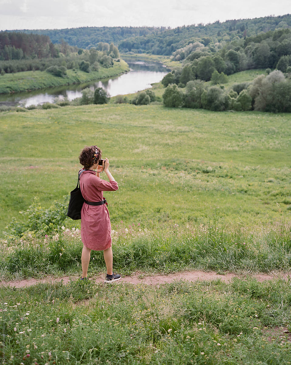 Young woman in burgundy dress with black bag taking picture on her camera