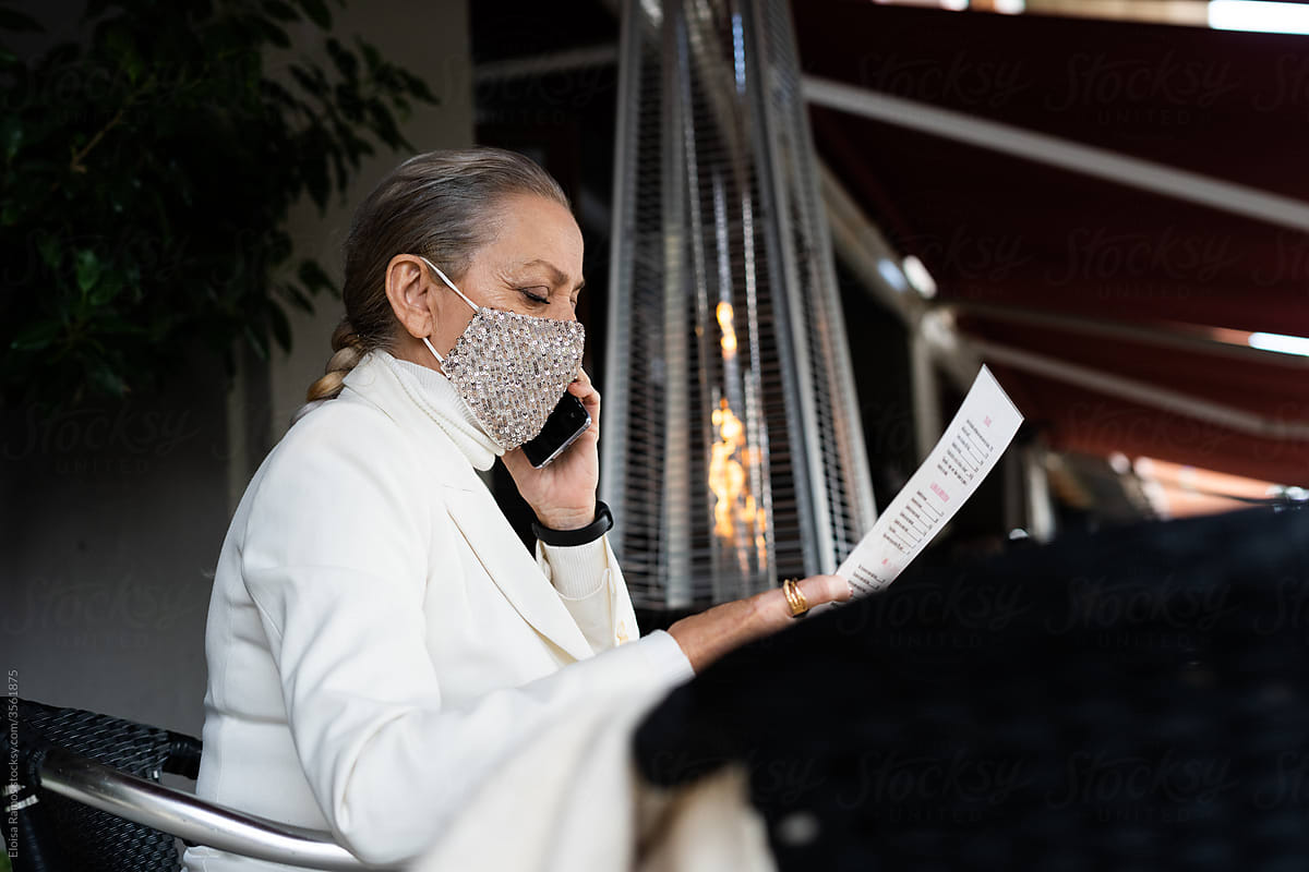 senior business woman reading menu, wearing mask at restaurant