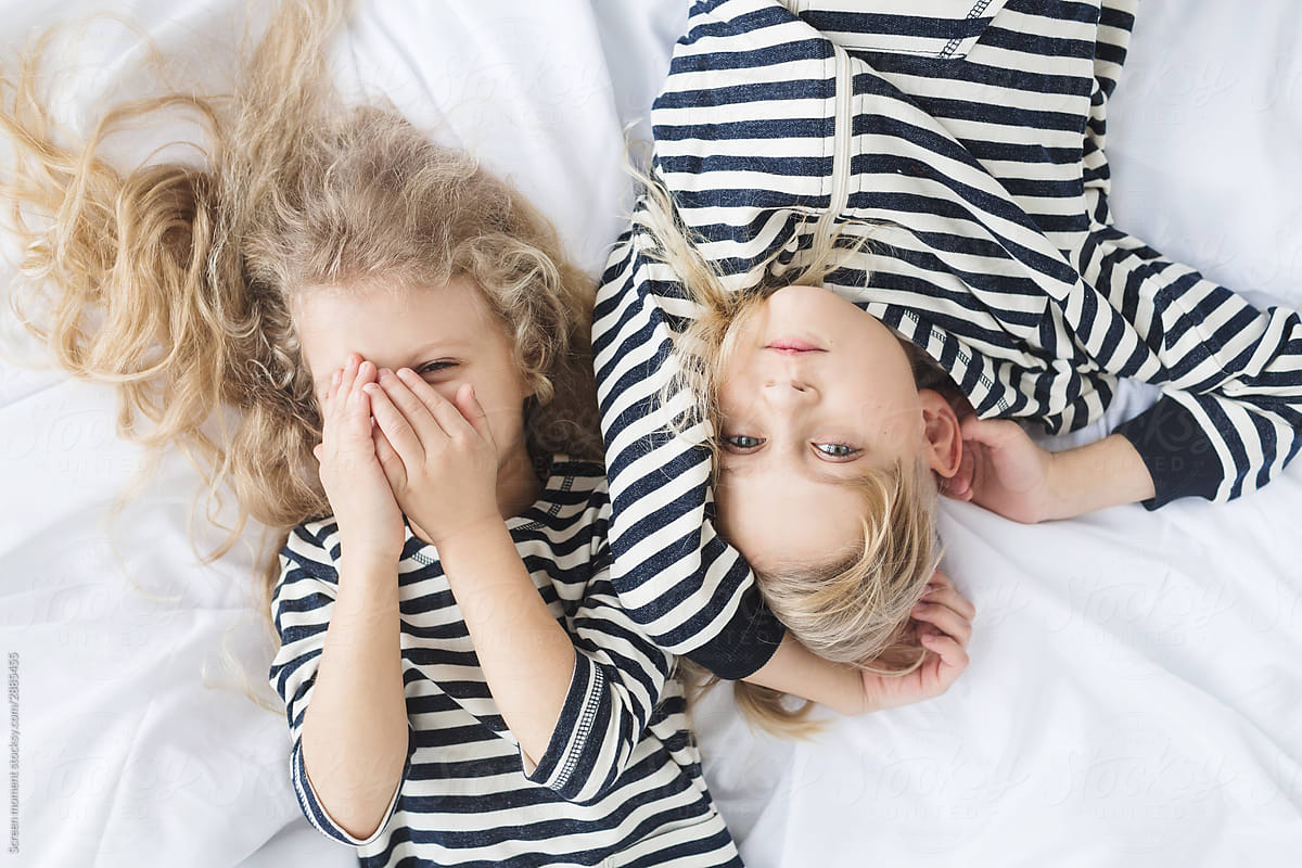 girl with white curly hair in a striped vest and a  boy with blond hair in a striped vest sleeping in bed.