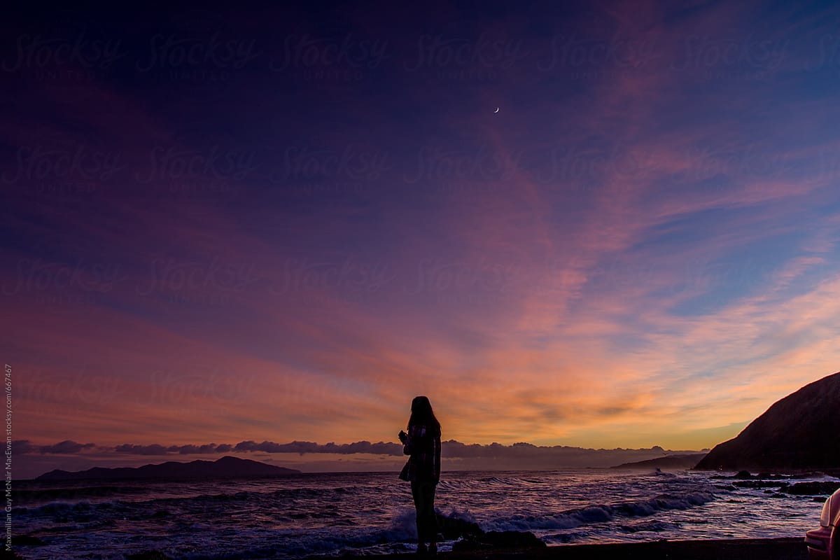 Silhouette of a young woman standing on the coast at dawn
