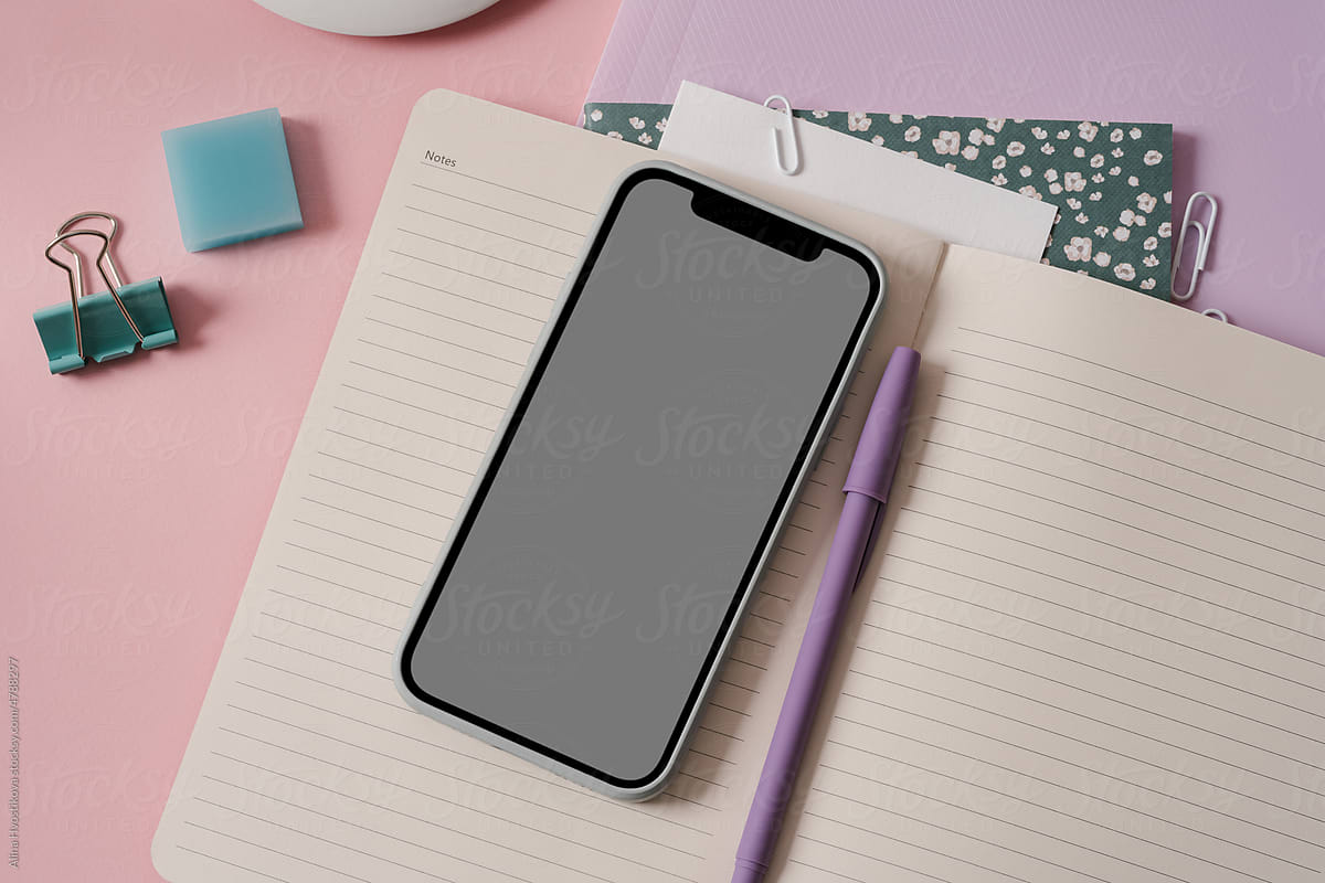 Smartphone with opened notepad arranged on pink desk