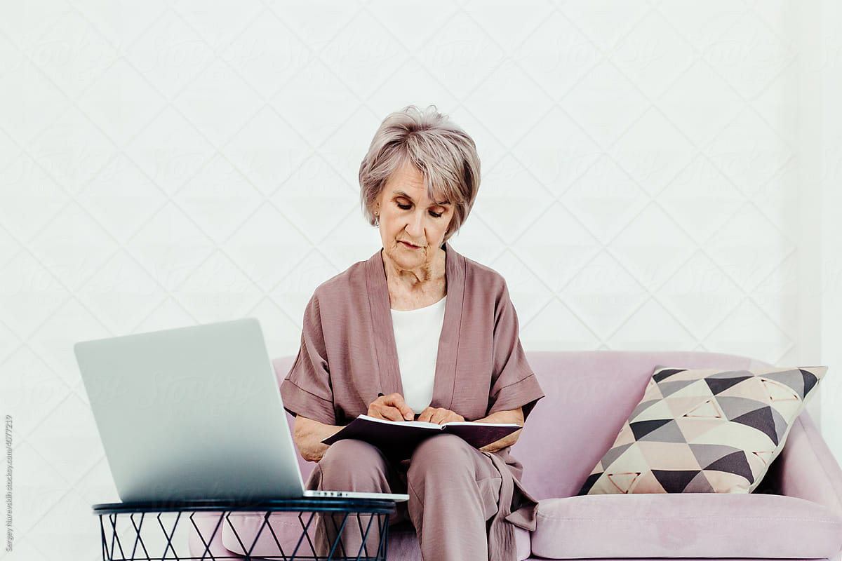 Senior woman taking notes using laptop at home