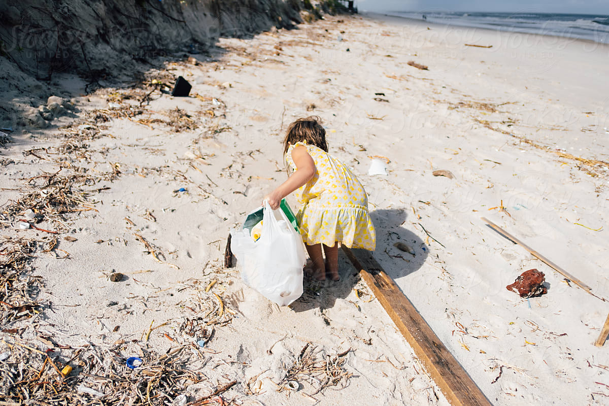 young child picks up plastic trash from beach