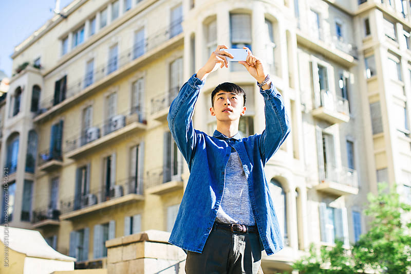 Stylish young asian man taking photos with mobile phone in the street.