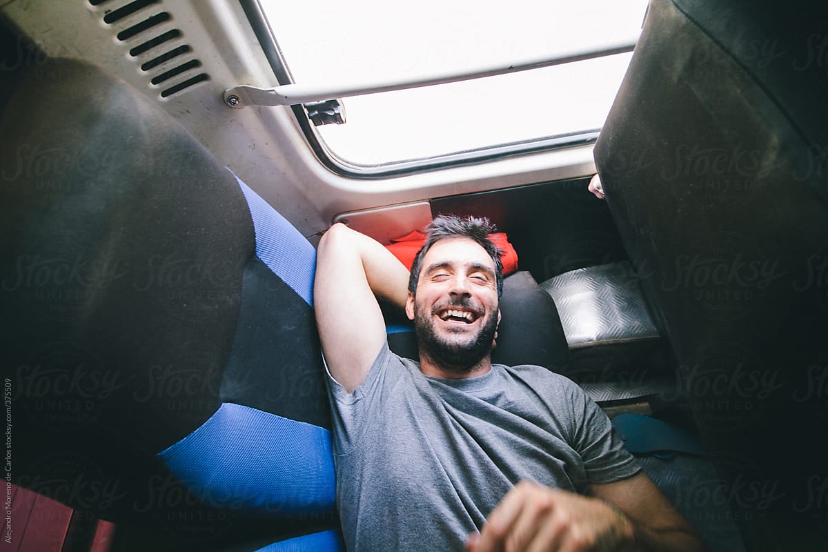 Young Man Laughing While Traveling On The Back Of A Mini Bus Lying Down On The Seats Del