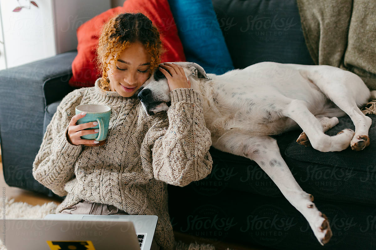 Teenager at home bonding with dog while using laptop