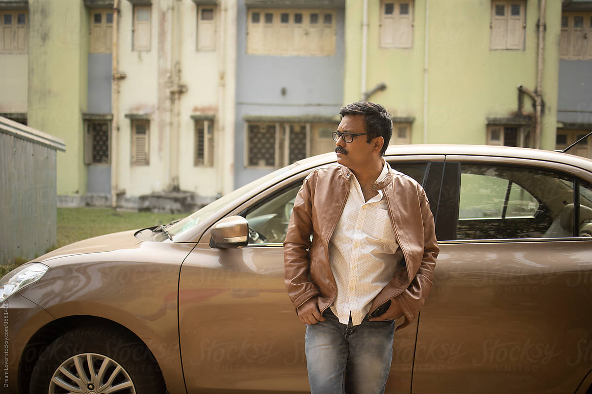 Middle aged Indian man standing in front of a luxury car
