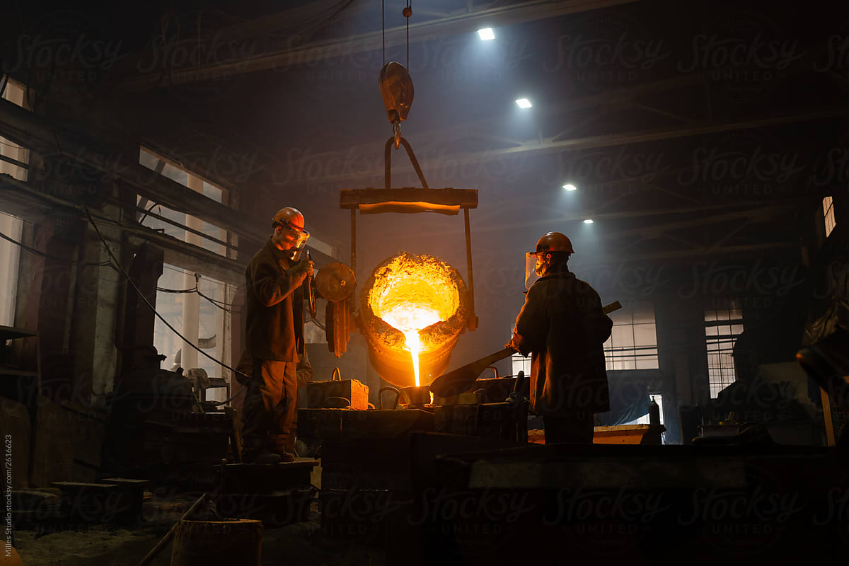 Men filling mold with metal in dark workshop