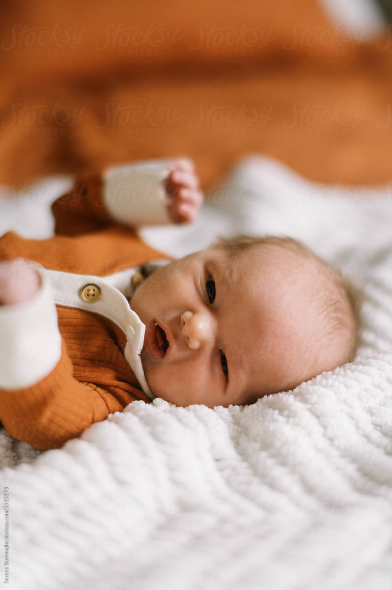 Awake newborn baby boy in orange clothing lying on bed at home