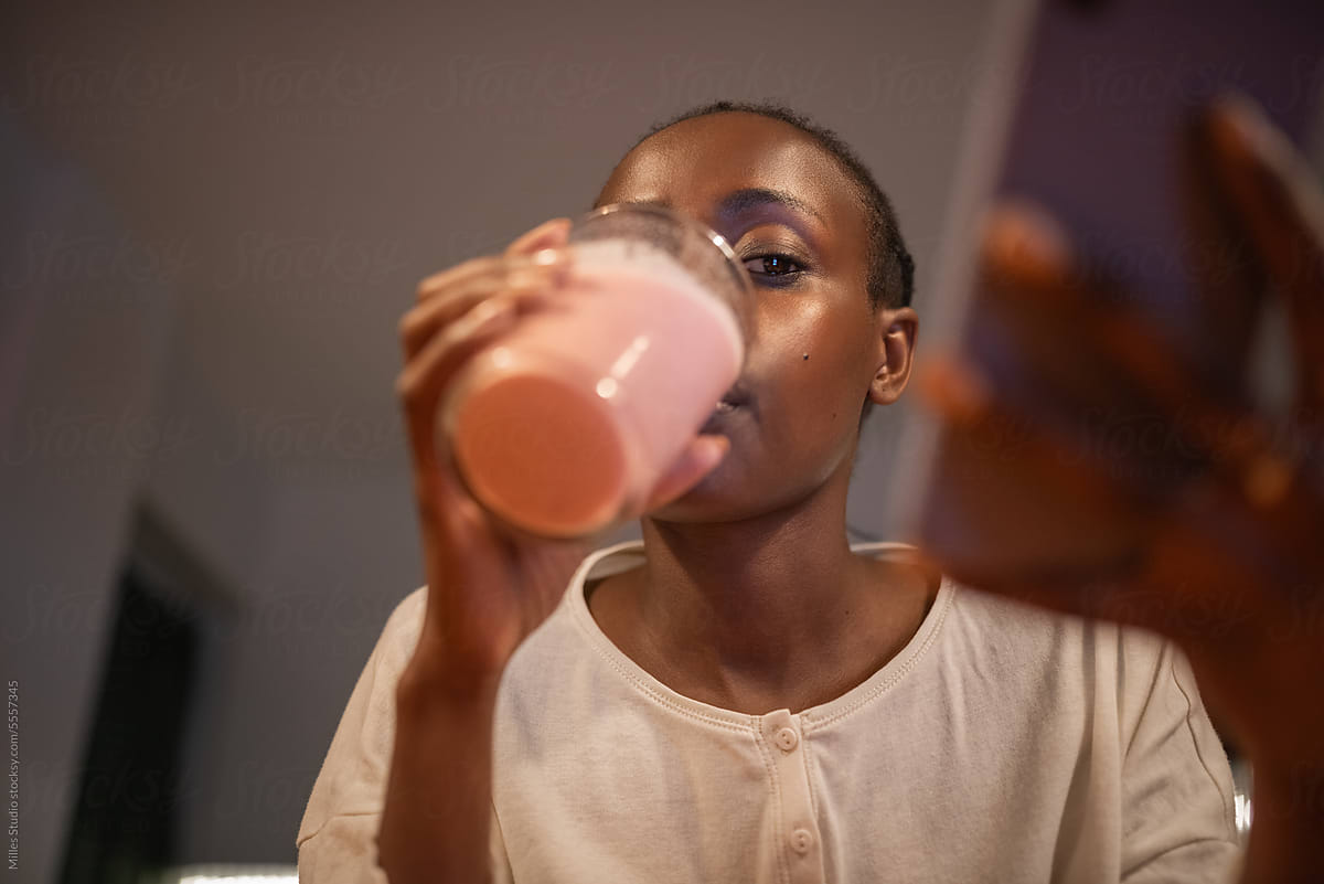 Black woman drinking smoothie and chatting via mobile