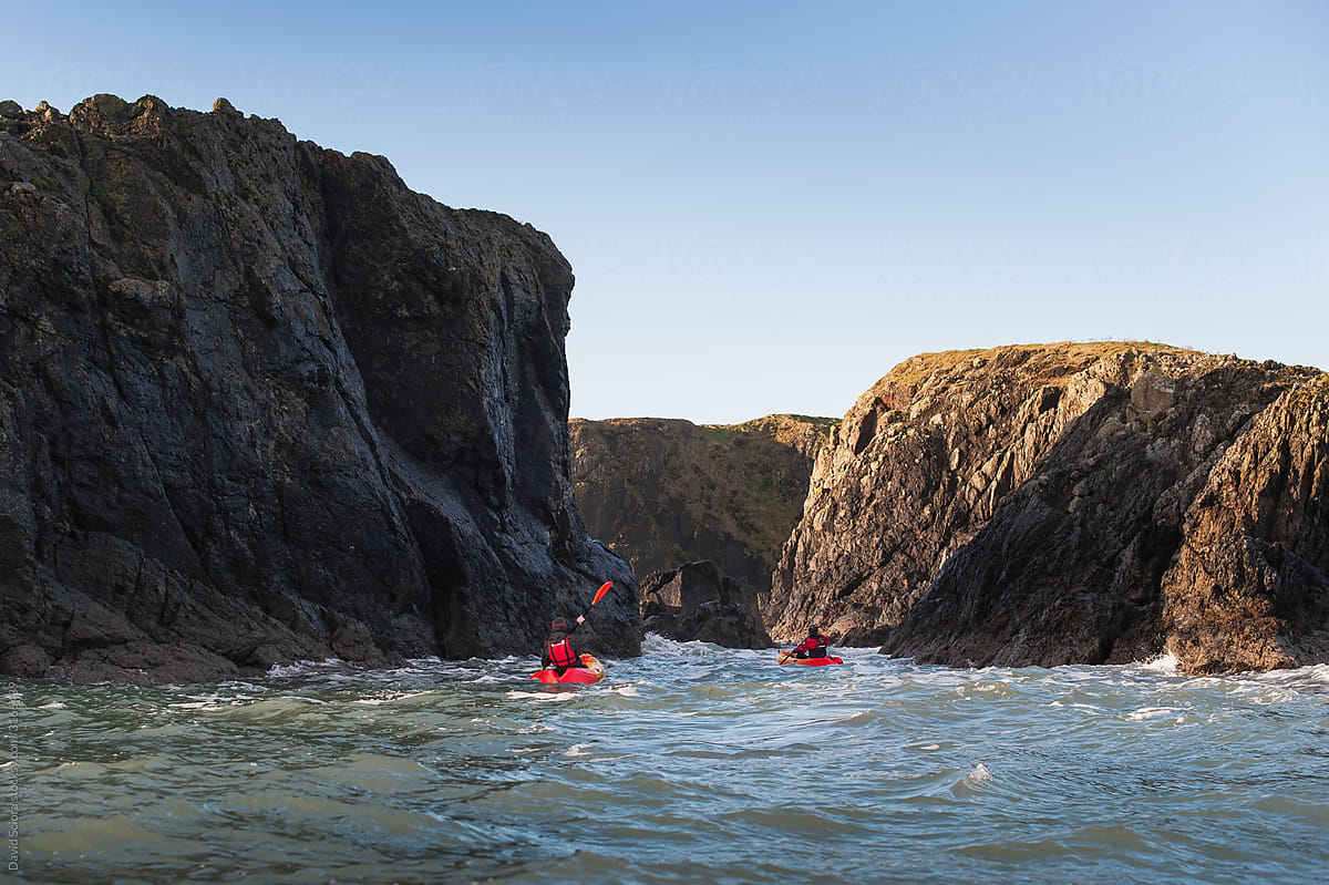 Two sea kayakers paddling between the rocks on a rough sea.