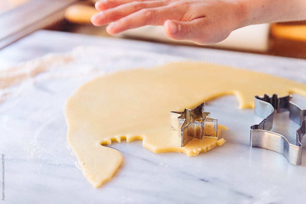 A child\'s hand using a cookie cutter to cut dough for Christmas cookies