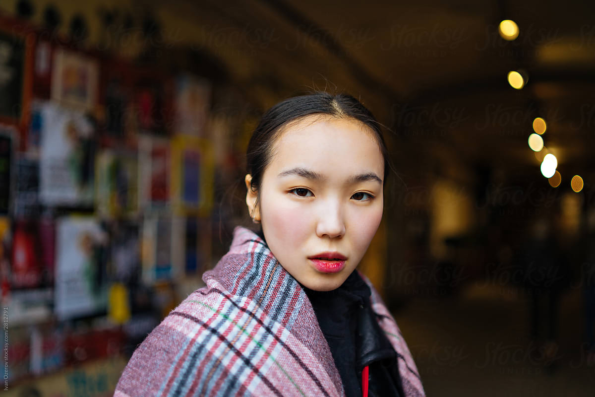 Adorable Asian girl in a plaid shawl against a wall with ads