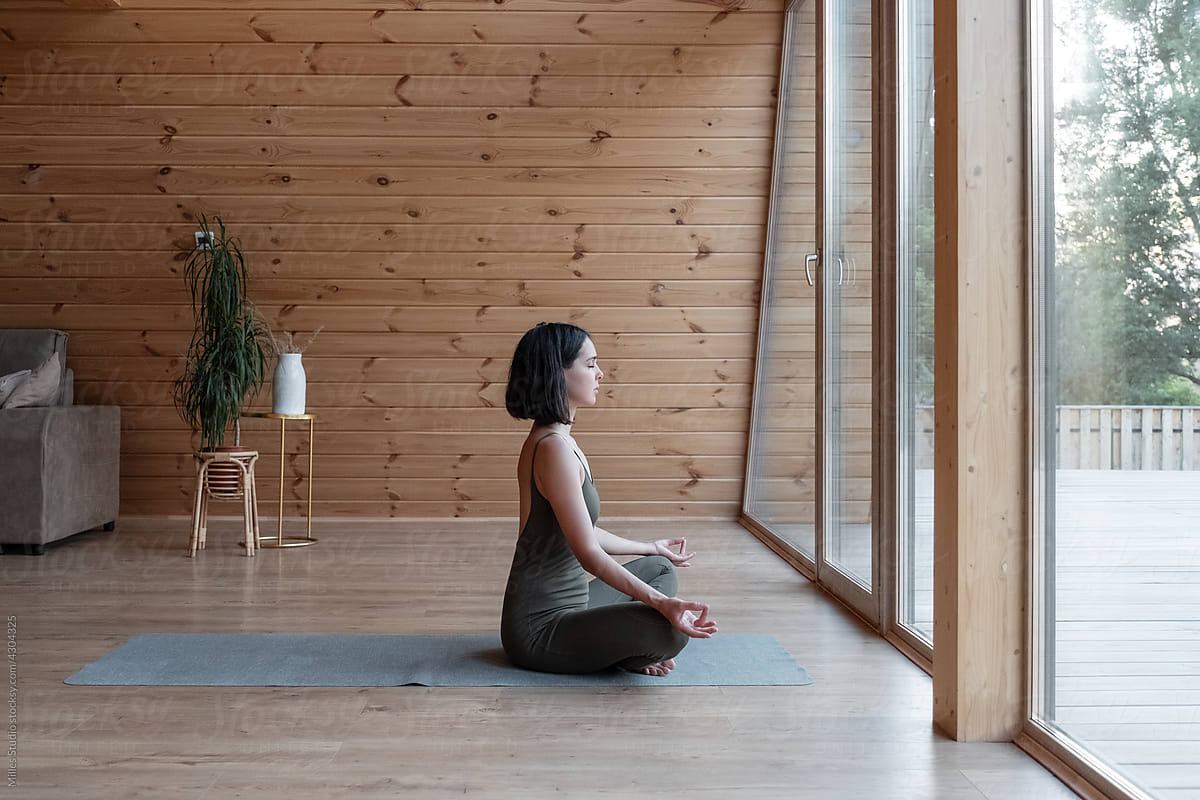 Woman meditating near window at home