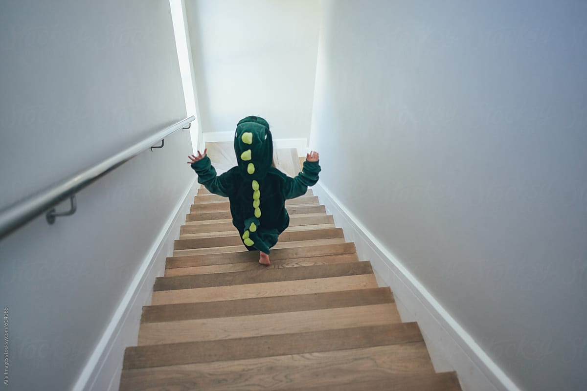 Cute little girl wandering around in dinosaur costume down the staircase