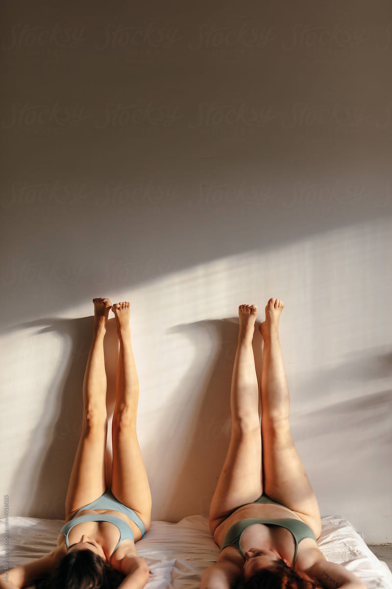 Two girls lying on the bed with their legs up (front view)