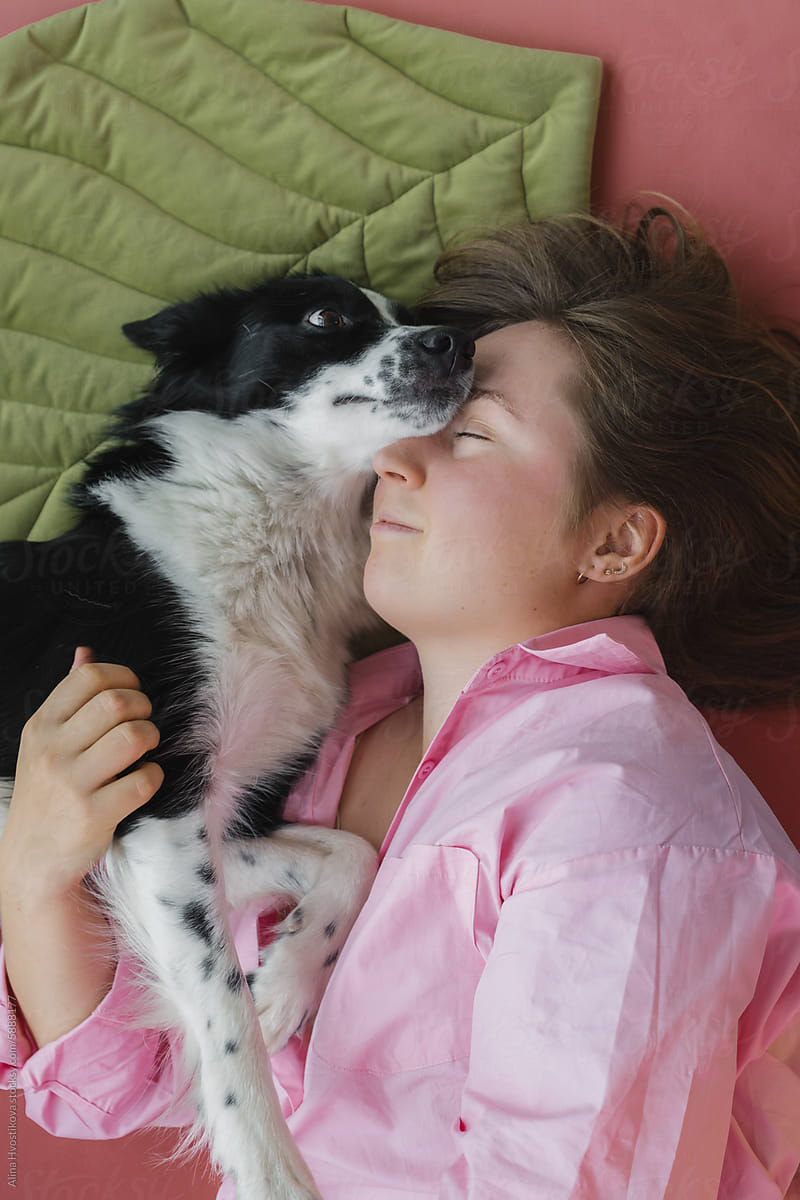 Happy woman with adorable dog lying on pink floor
