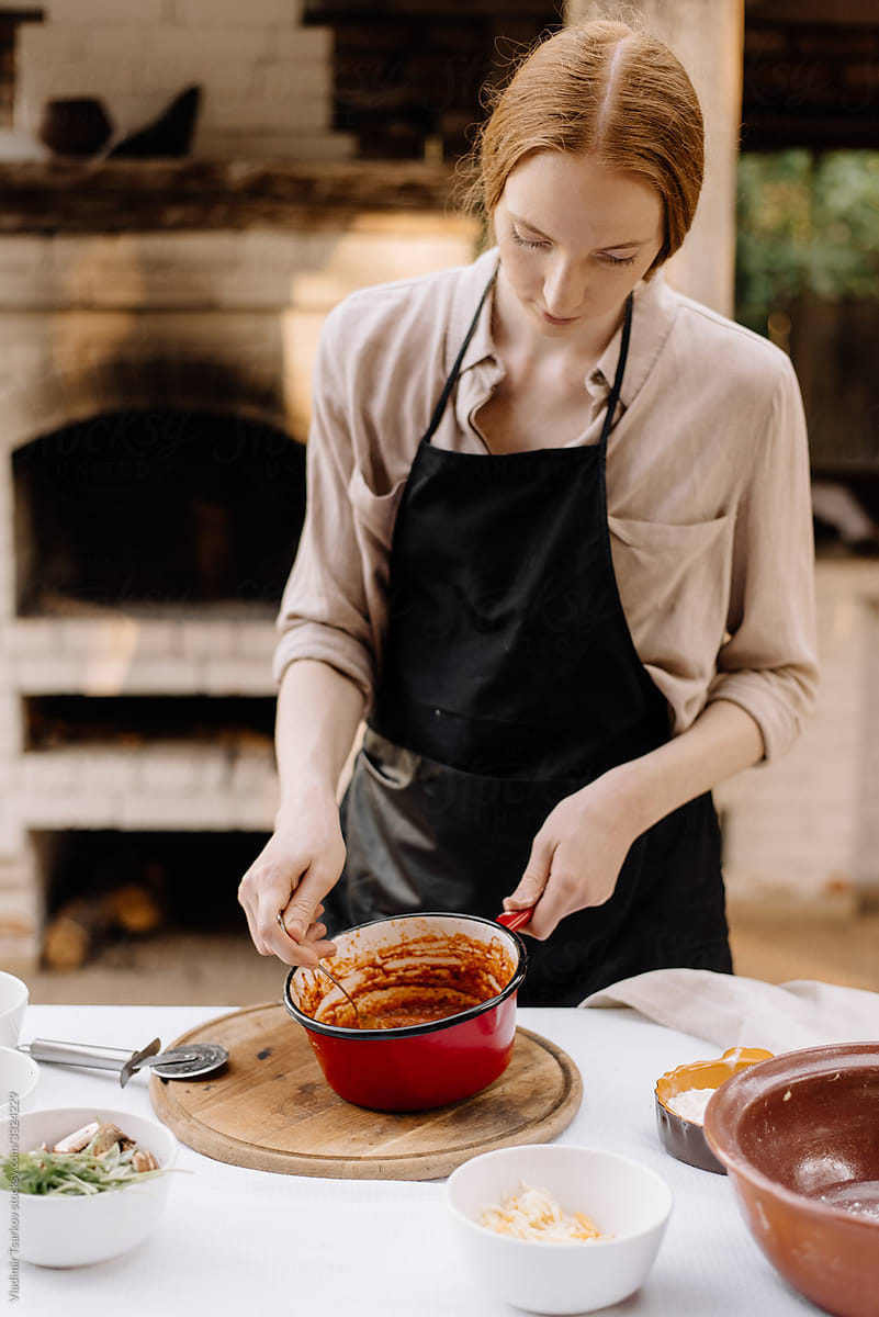 female chef prepares stirring tomato sauce