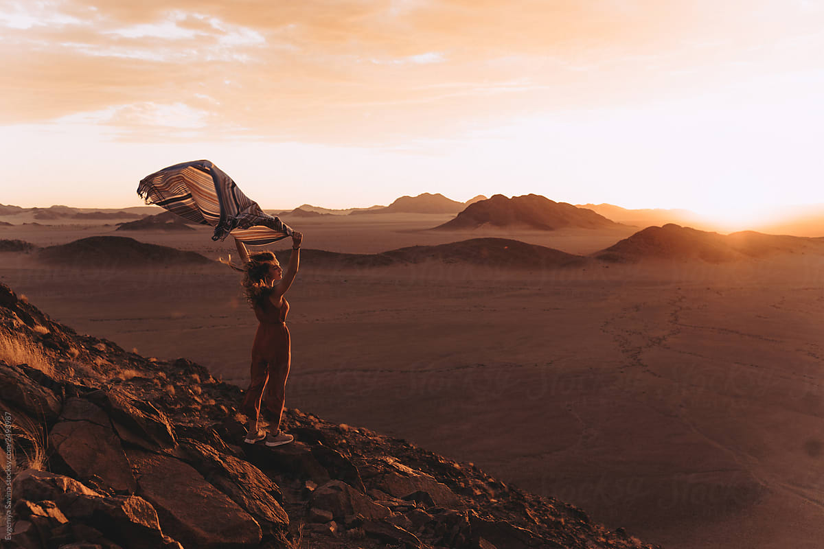 A sunset in Namibian desert and a girl with a scarf standing