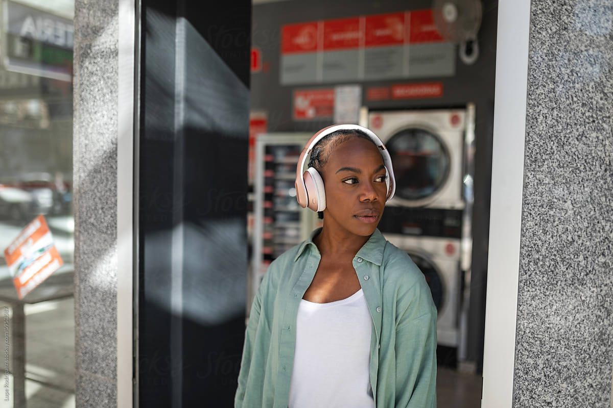 portrait of black woman with headphones at the door of a laundromat