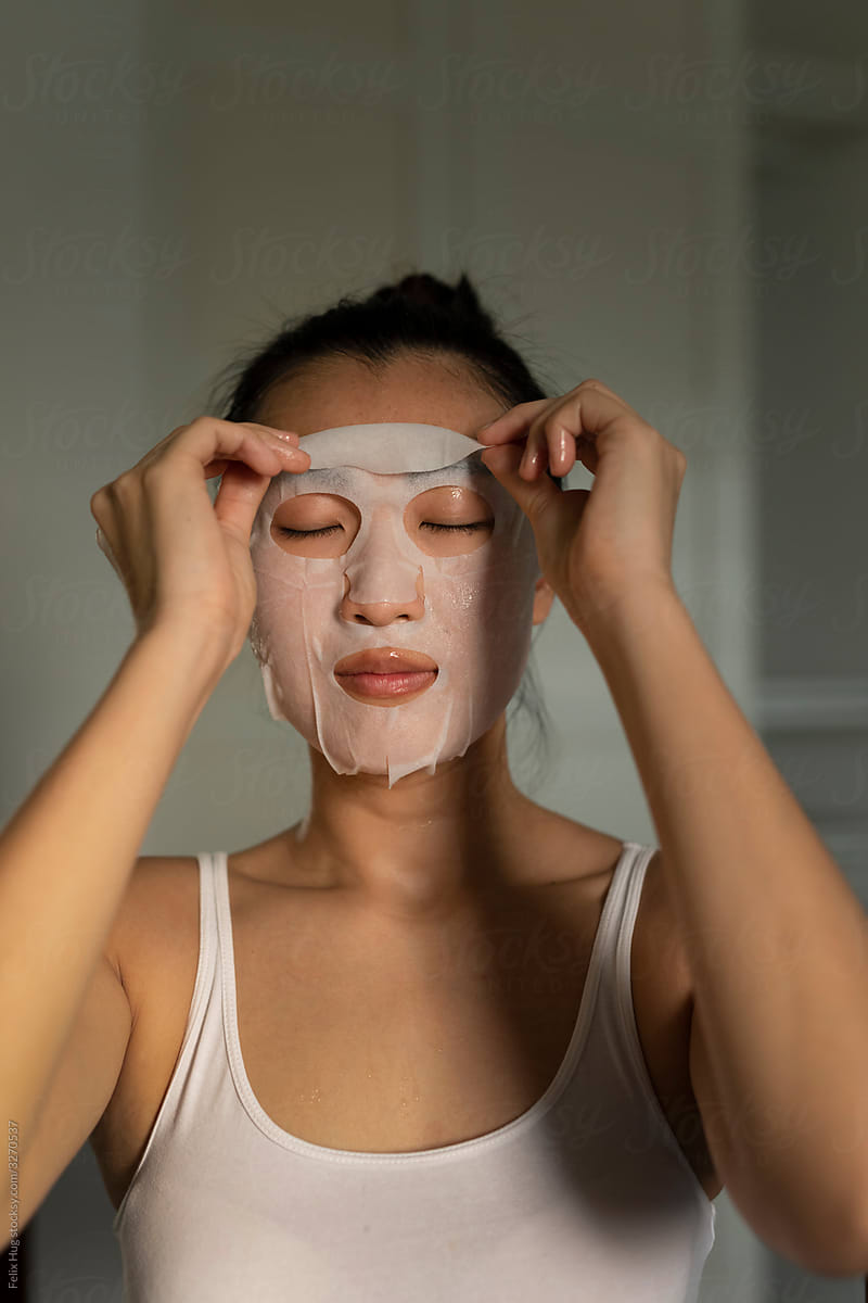 Portraiture of a young Singaporean woman taking off a moisturised face-mask