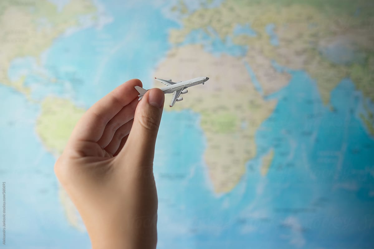 Close up of person holding a small airplane in front of the world map