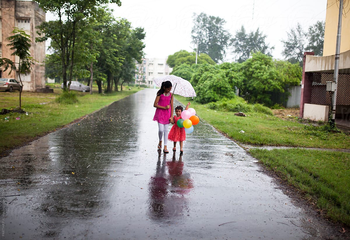 Sisters walking through wet road with balloons in hands