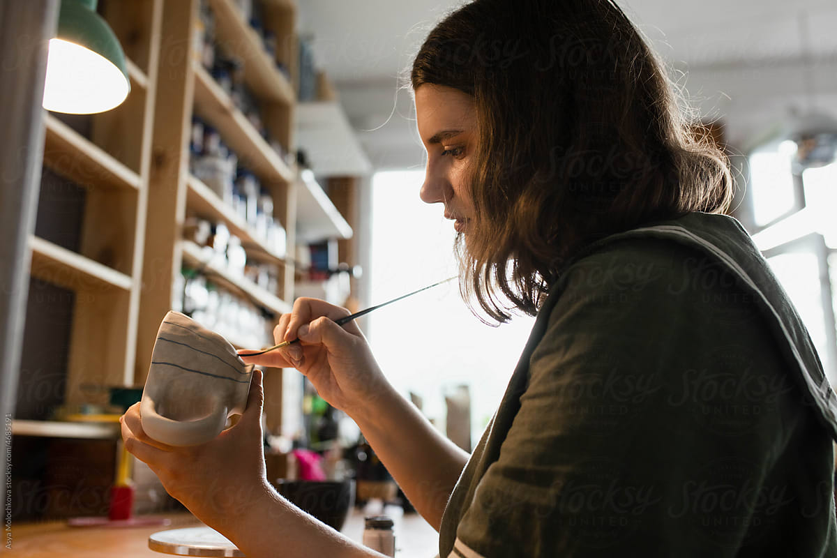 Portrait of woman ceramist applying paint to clay mug