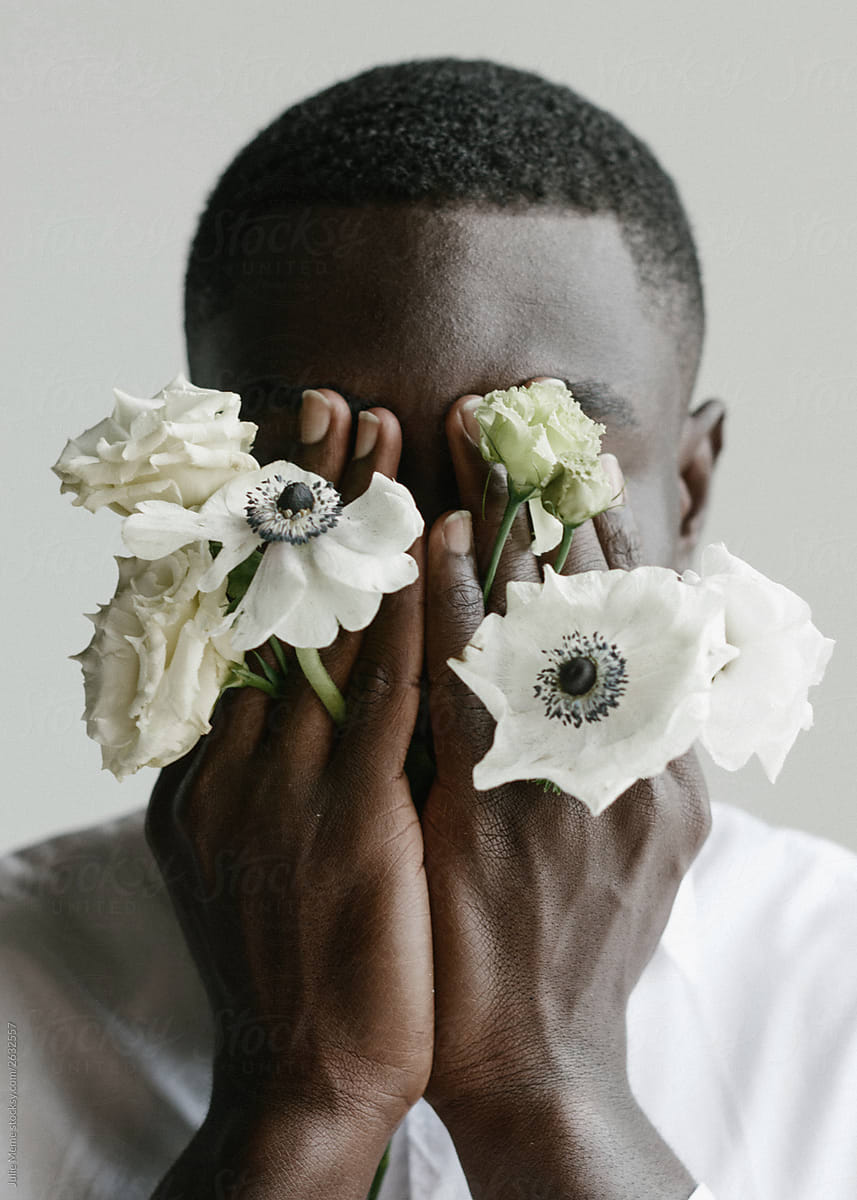 Portrait of handsome african guy who\'s covering his face with his arms and flowers through his fingers