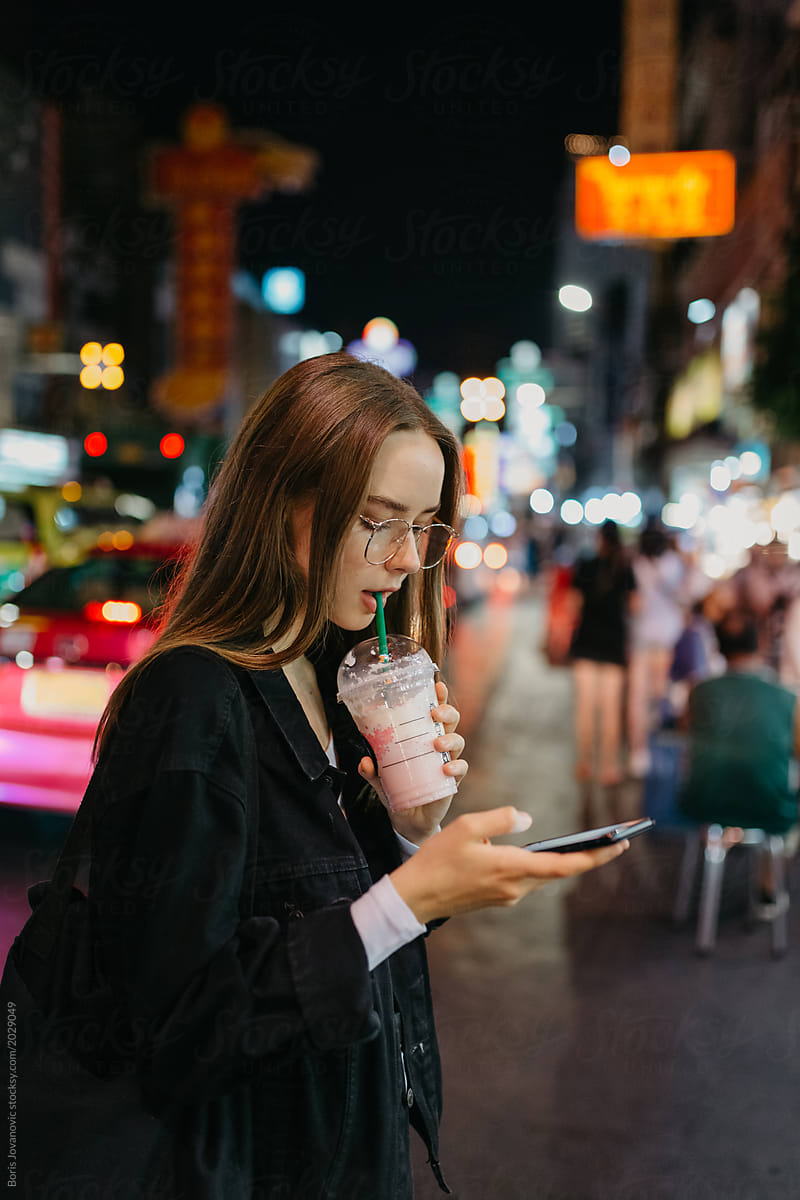 Young woman using a mobile phone on the street and drinking a milkshake