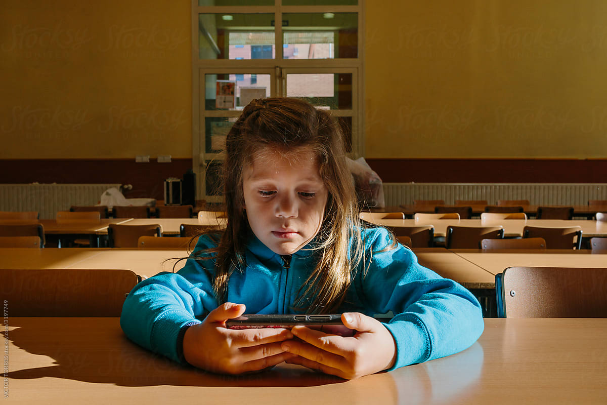 Little girl watching videos alone on phone in an empty classroom
