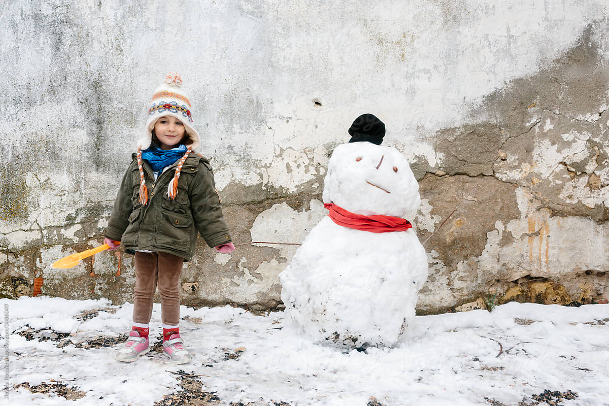 Little girl smiling posing next to a snowman over old broken concrete wall