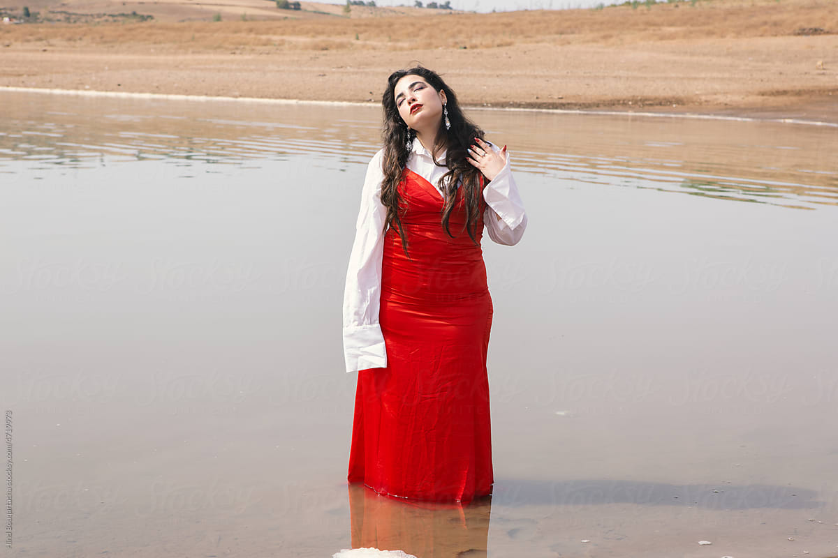 beautiful girl with long hair wearing red dress standing on the river