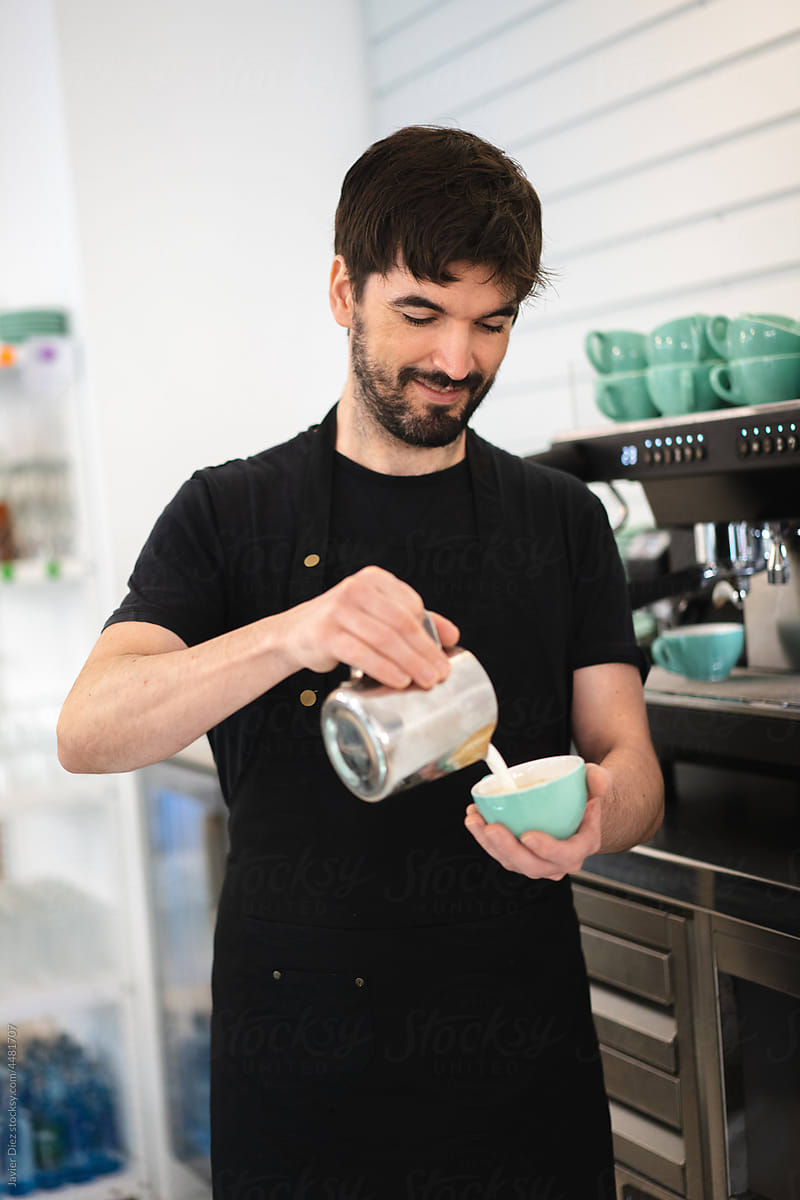 Barista adding milk to coffee during work in cafe