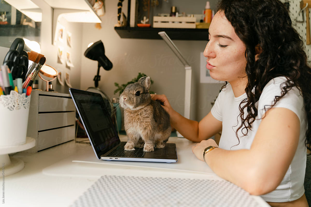 young woman petting her rabbit/bunny, distracting her from work