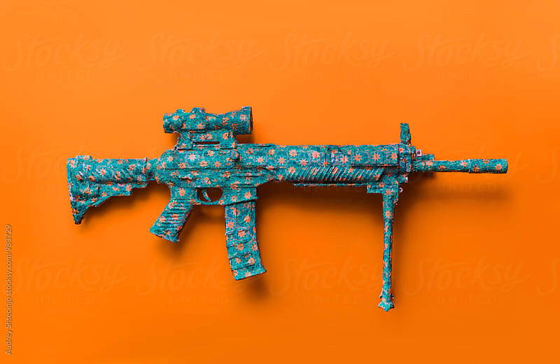 Automatic gun covered with decorative paper on orange background.