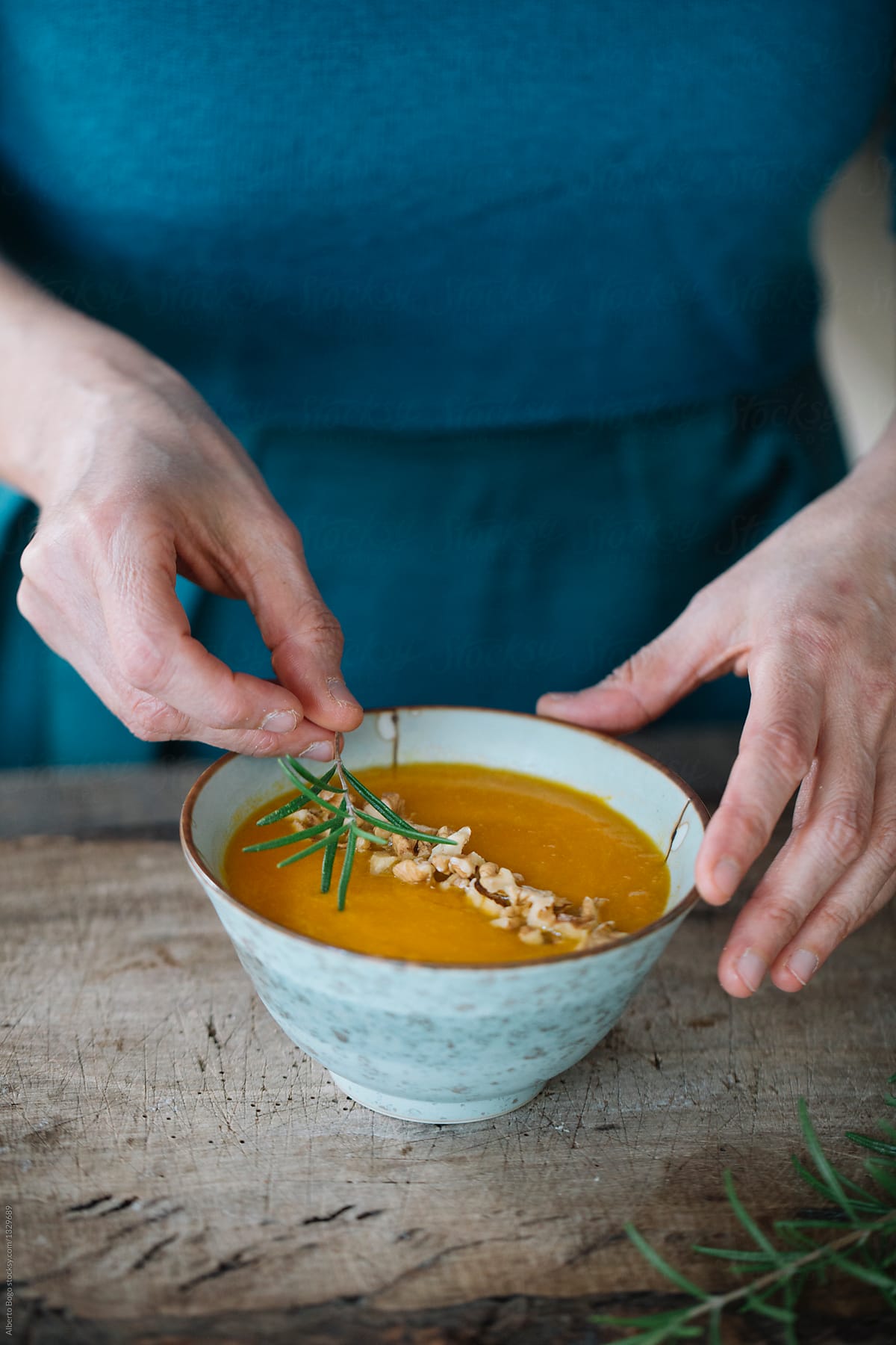 Person decorating soup with rosemary and walnut