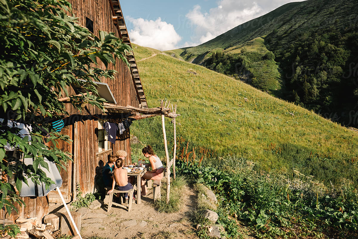 group of kids and teens  eating dinner outside a hut in the Alps