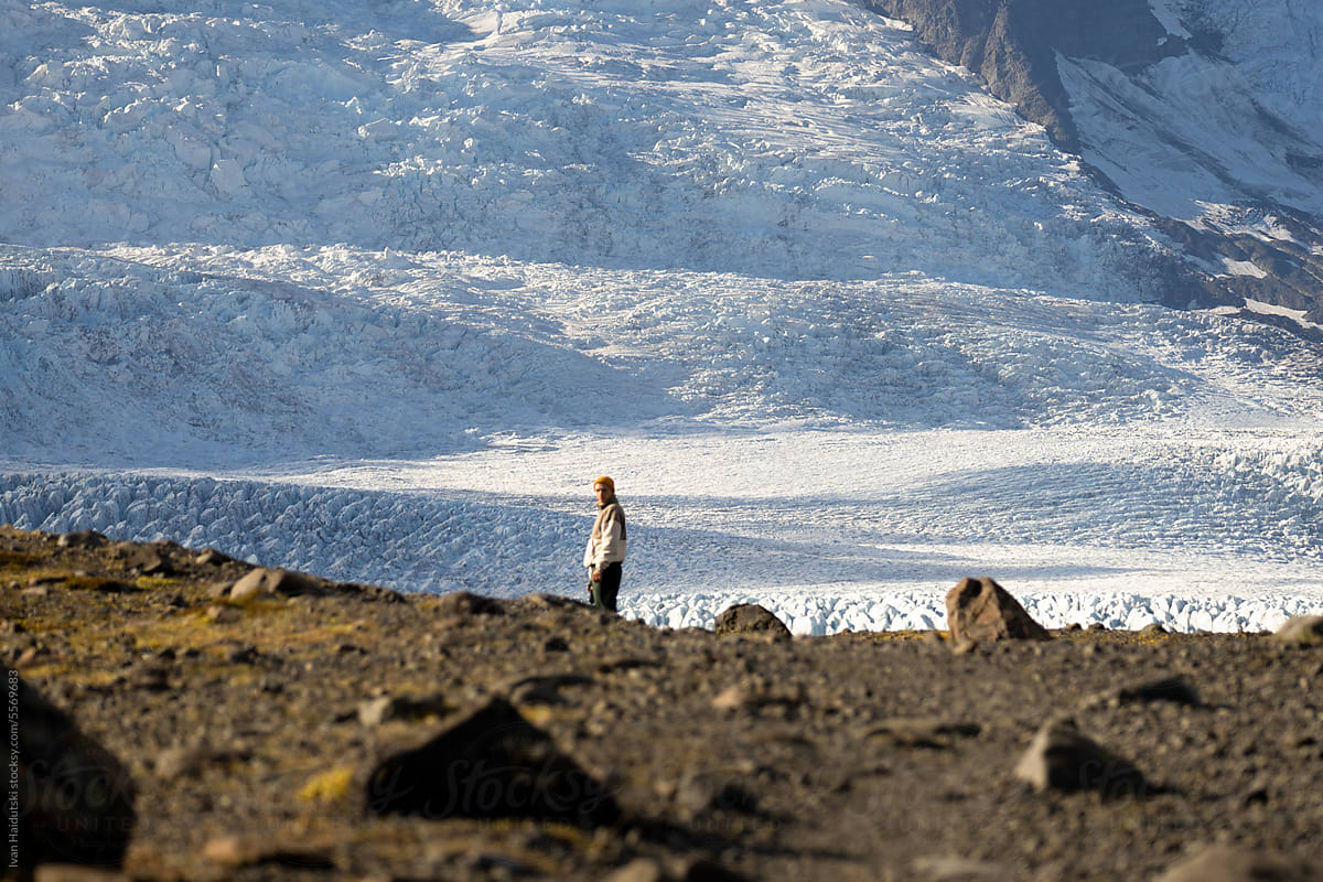 young man from behind holding camera in hands walking to huge glacier