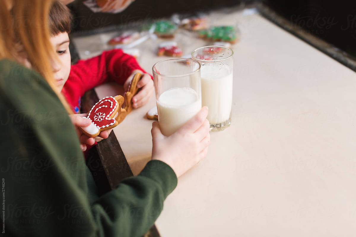 Children drink milk and eat Christmas cookies in the kitchen in holiday sweaters with deer