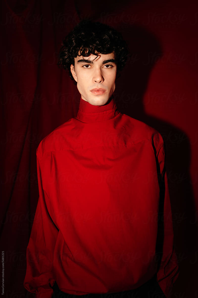 Young man in red dress standing in maroon wall room