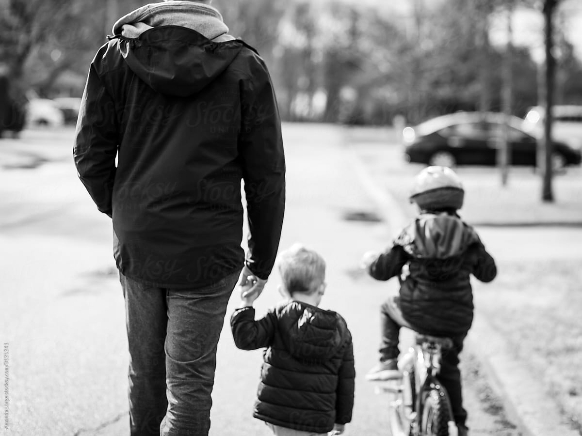 two young boys bike with their father in a suburban neighbourhood.