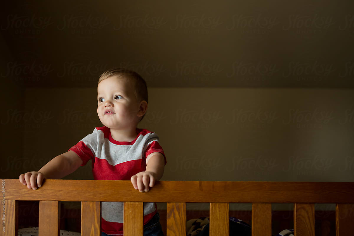 Toddler boy peeks over bed rail