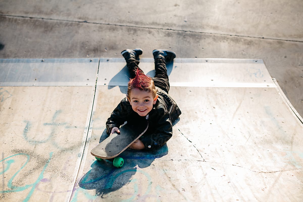 Smiling punk kid lying on ramp with skateboard.